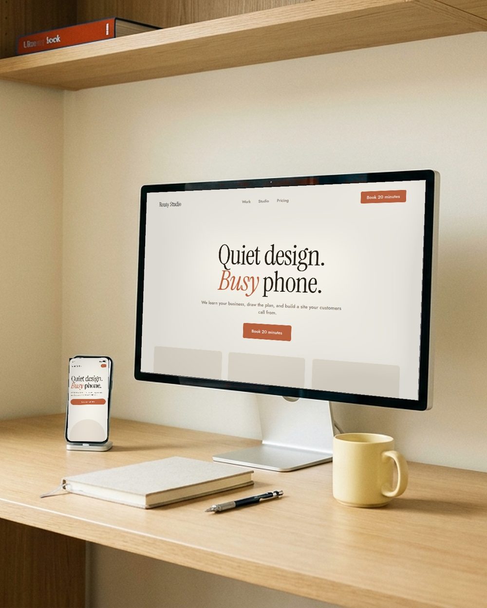 The studio desk: a monitor and a phone showing the same site, a notebook, a mug